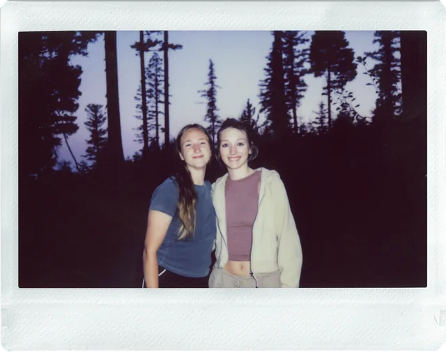 Instax Wide print of two friends among pines at dusk